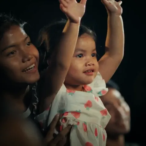Woman holding her daughter up, who has her hands in the air. Both are smiling.
