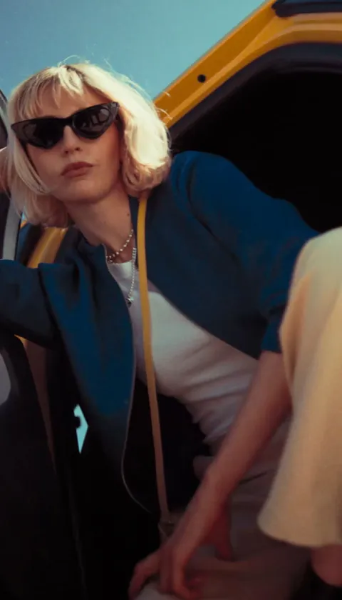 A lady hanging out of a Ford Capri wearing black sunglasses and a blue jacket.