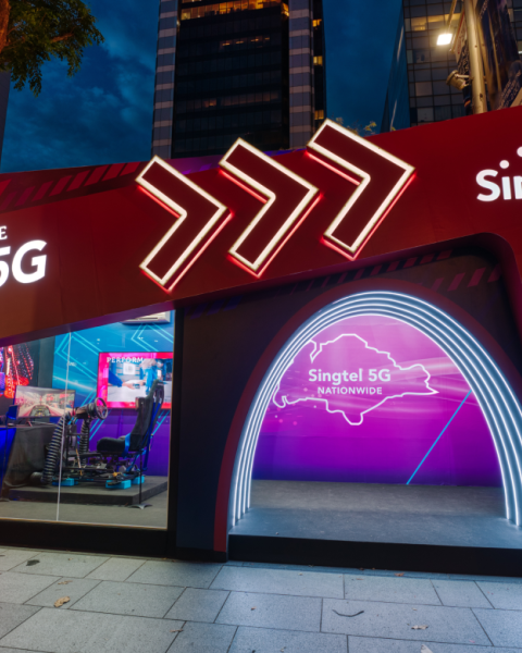 A Singtel store brightly lit at night, with arrows on the front of the store pointing right.